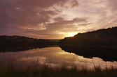 Damflask reservoir at sunset with a dark orange to pink sky reflected in the water