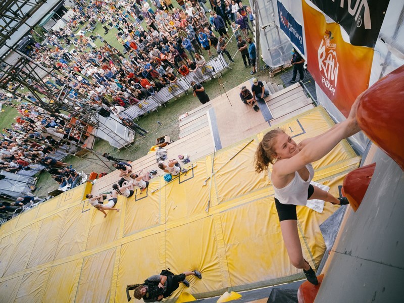 Cliffhanger - woman scaling a climbing wall in front of an audience