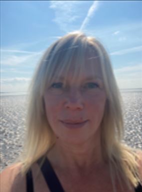 Photo of Helen Sanders.  Shoulder length straight blond hair.  Beach and blue sky in the background