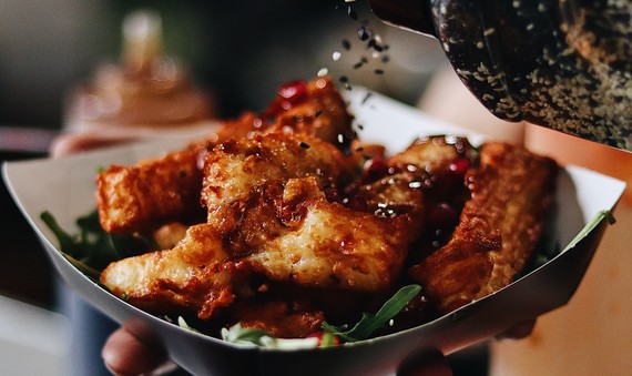 Halloumi fries in a recyclable paper plate being topped with toasted sesame seeds