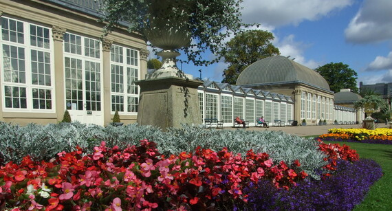 The glass house Pavilion building at Sheffield Botanical Gardens. Beds of colourful flowers run along the perimeter of the lawns.
