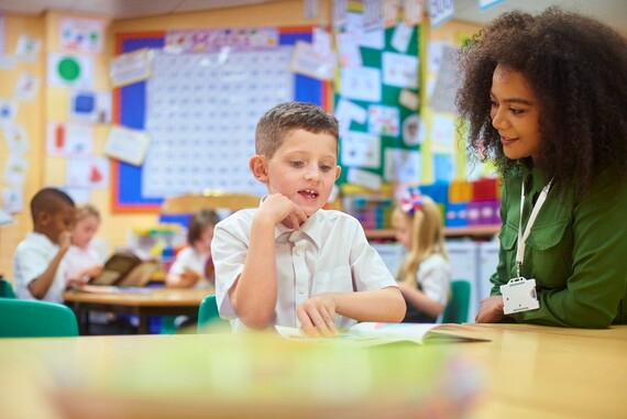 Smiling volunteer listens to a child reading in a library.