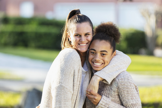 An adult standing outside with their arm around a young person, both smiling at the camera