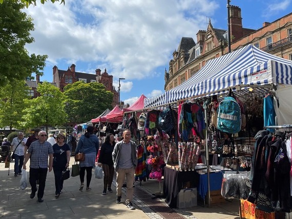 A bustling outdoor market scene with stalls and people browsing in the sunshine