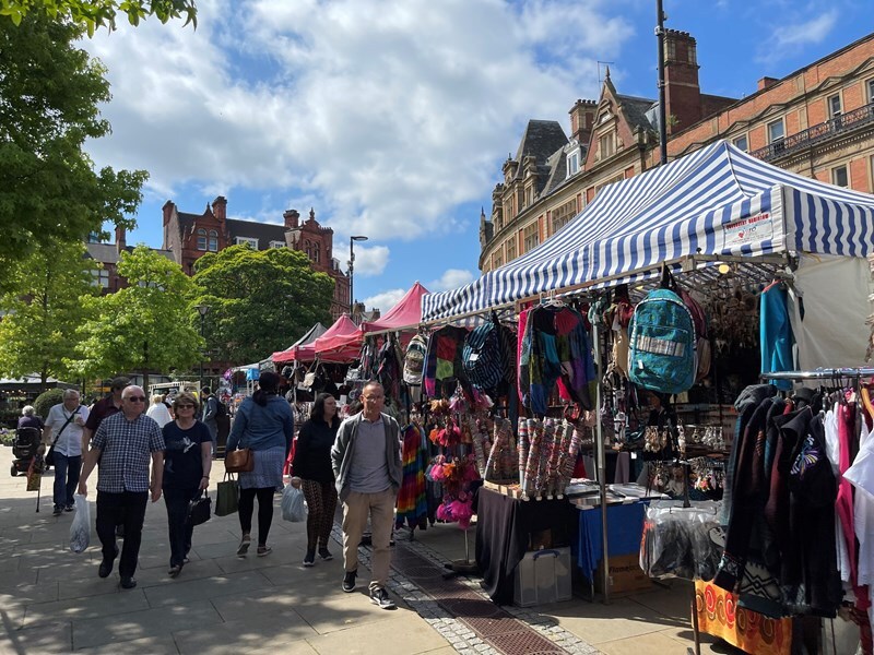 A bustling outdoor market scene with stalls and people browsing in the sunshine