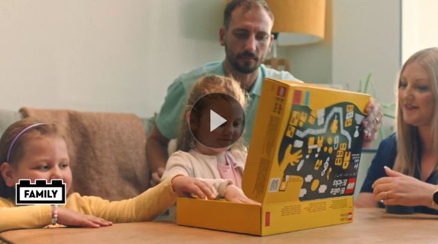 Opening picture of video showing a man, a woman and two young girls opening a box of braille lego