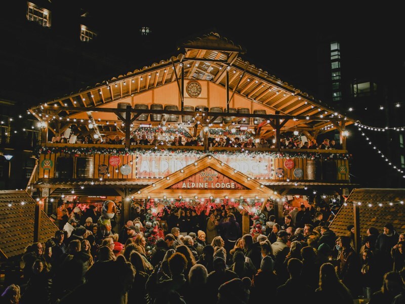 The Christmas Market's Alpine Lodge bustles with crowds enjoying the festivities on a cold winters night. 