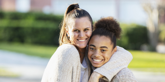 Adult and child stand outside with arms around each other