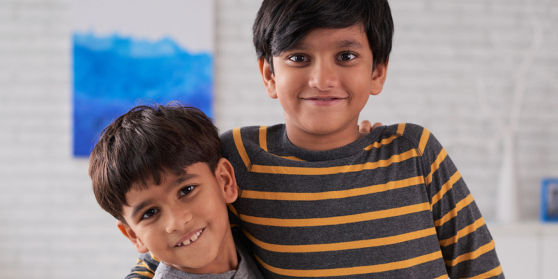 Young siblings stand together inside with their arms around each other looking happy