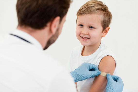 A doctor wearing a white coat is applying a plaster to a smiling child. Image by Freepik