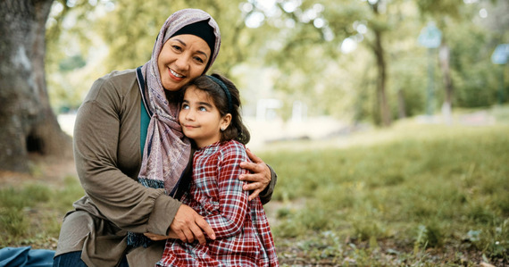 An adult and child sit happily together in a park