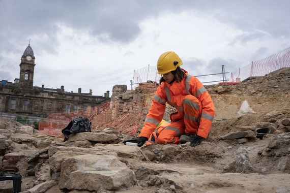 A Wessex archaeologist in an orange boiler suit and hard hat trowels back deposits at the Sheffield Castle dig