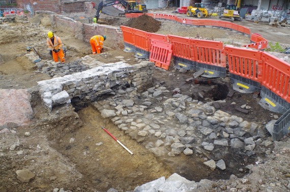 Archaeologists in orange boiler suits and hard hats work on a large uncovered part of the Sheffield castle wall