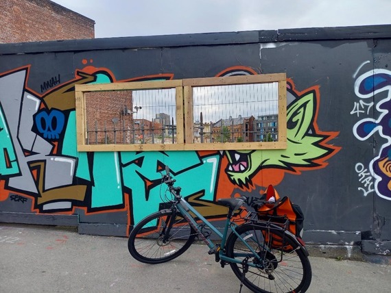 A bike is parked in front of the castle site's graffitied hoarding where a new window panel has been installed.