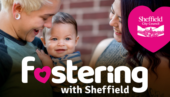 Two adults stand close together outside. They are both smiling down at a baby one of them is holding. The baby looks happy.