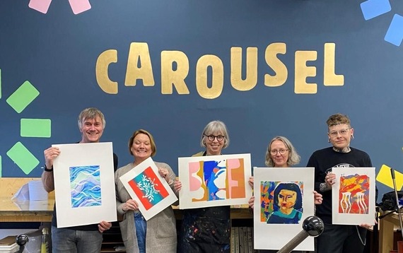 Course attendees show off their artwork in front of the Carousel sign