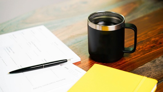 cup of coffee next to notepad and pen