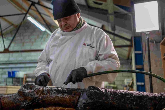 A Civil War stake is being cleaned by a timber specialist from York Archaeology who is wearing gloves, a woolly hat, and a white overcoat.
