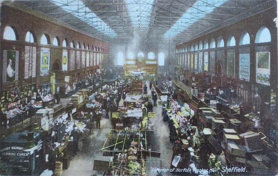 An old image of Norfolk Market Hall taken from above, with wares piled high and people browsing.