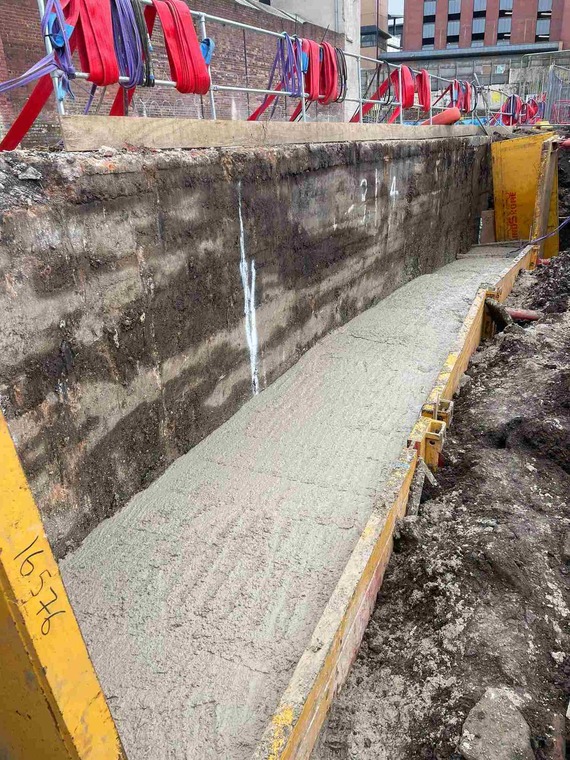 Fresh concrete has been poured into a trench box next to the culvert wall.