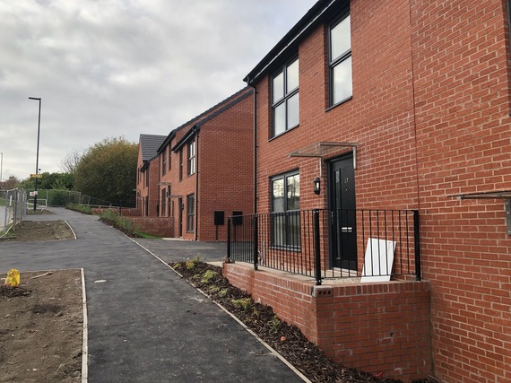 A brand new, orange-brick council house with a pathe running past it. There are two more similar properties in view on a grey, cloudy day.