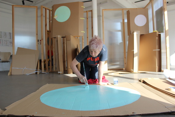 Emma Bolland paints a turquoise circle onto cardboard on a studio floor.