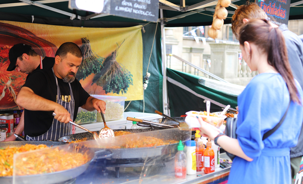 A food vendor cooking a large dish with customers about to be served