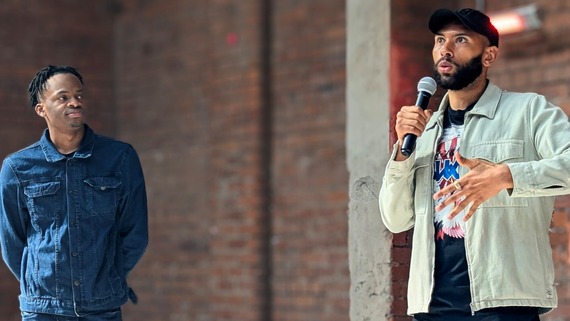 two men standing and giving a speech holding a microphone