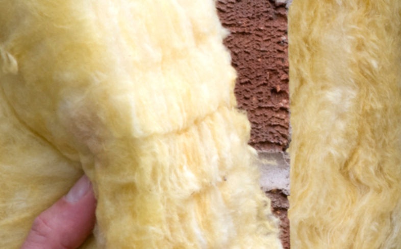 A close up image of fibre loft insulation being held up against a brick wall