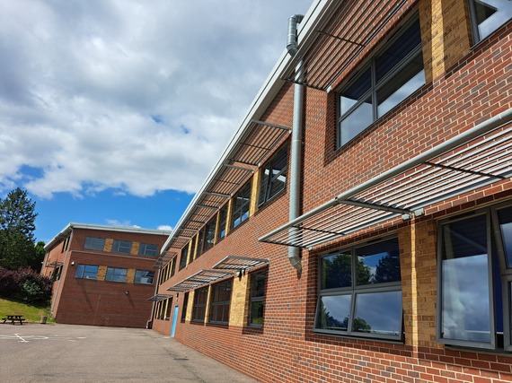 A red brick two-storey school building with shades above the windows. Above the building the sky is blue with fluffy clouds.