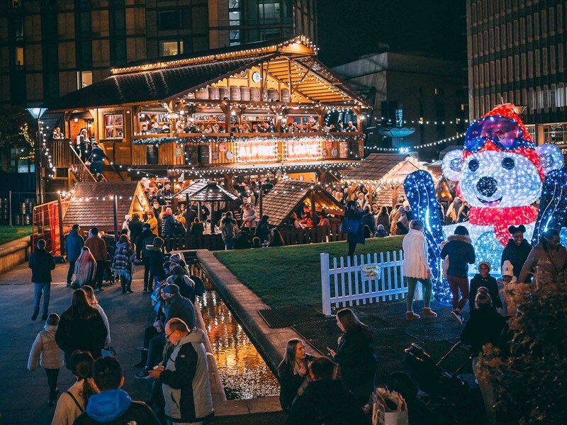 Festive Christmas market at night with a large wooden chalet lit by string lights and a glowing polar bear decoration.