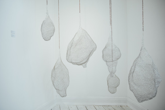 Intriguing mesh-like sculptures with undefined shapes dangling from ceiling in a white gallery space.