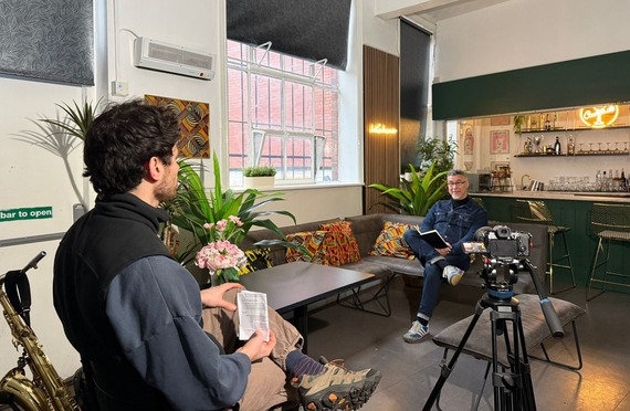 Person interviewing person on camera whilst sat amongst plants and patterned cushions.
