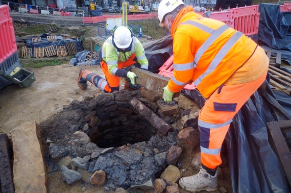 Two people in orange high-vis jackets remove stones from the top of a newly discovered well on the Castlegate site