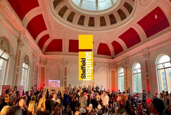 A crowd inside Canada House with musicians onstage and the Sheffield Inspires logo in the centre