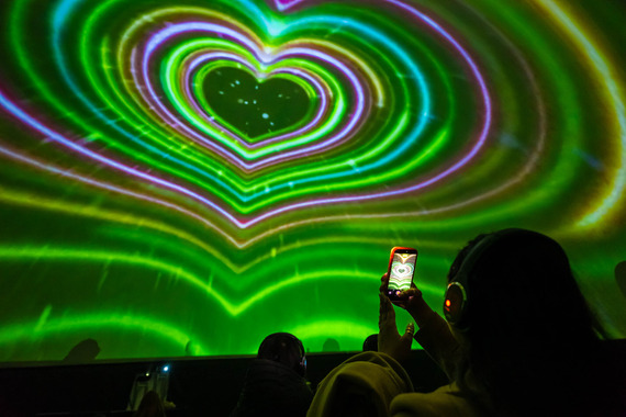 A shot inside Planetarium Go UK's mobile unit. A person holds their phone in front of a screen, showing vibrant coloured love hearts.