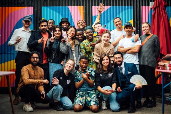 A large group of people pose together for a group photo in front of a colourful, patterned backdrop made of bright panels with abstract shapes.