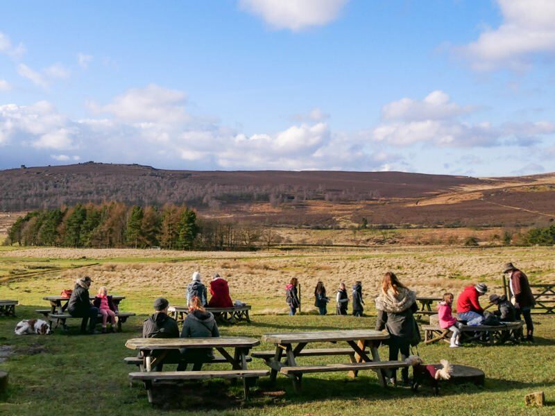 People sitting on picnic benches in front of views of the Peak District
