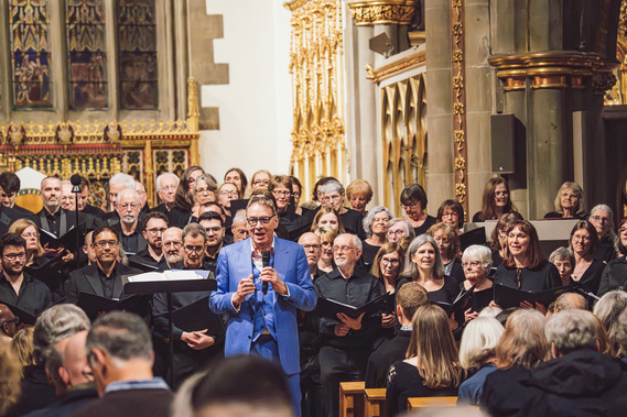 A chorus led by a blue-blazered man in a cathedral.