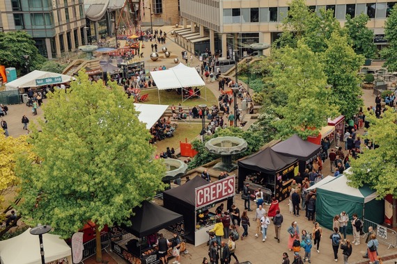 Aerial view of Sheffield food festival with market stalls, trees, and people walking between tents and buildings.