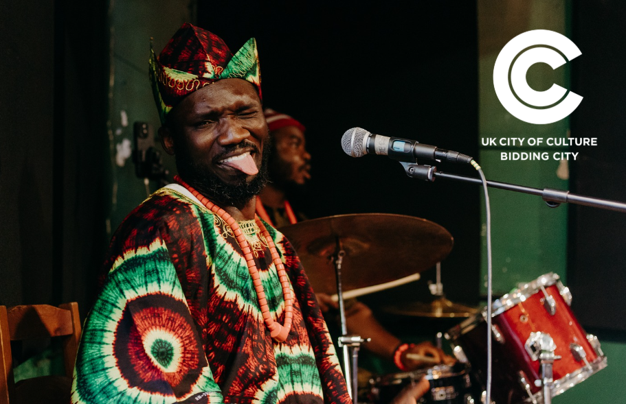 Person in vibrant African dress with tongue out, next to a City of Culture logo overlay.