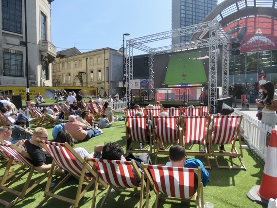 Crowds sat on deckchairs at Tudor Square. They are watching the snooker on a big screen.