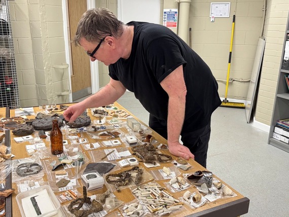 A man in a black t-shirt wearing glasses looks over the archaeological finds from the Sheffield Castle site