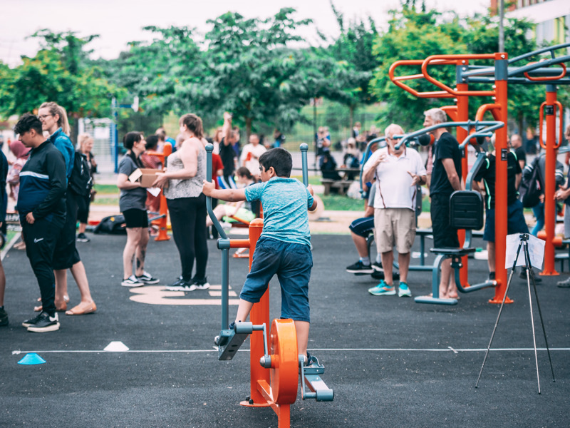 A number of people enjoy activities in a playground, with trees in the background.