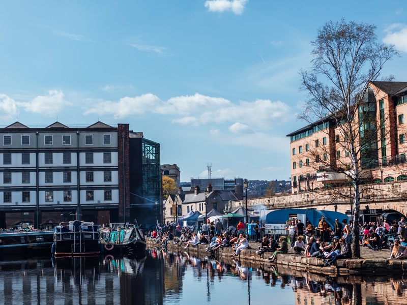 Victoria Quays in Sheffield, with people along the side of the water. There are canal boats, cobbled streets and buildings also visible.