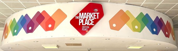 Colourful overlapping tag shapes around a red “The Market Place Crystal Peaks” sign above a shop entrance ceiling.
