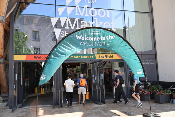 A banner in front of the Moor Market entrance. People walk through the doors.