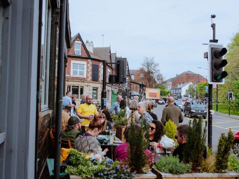 People congregate outside of a bar in Abbeydale Road. There are buildings in the background.