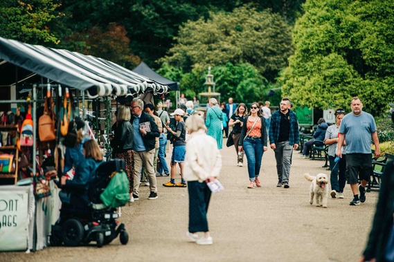 Visitors walk past stalls lining a path at Art in the Gardens in the Botanical Gardens.