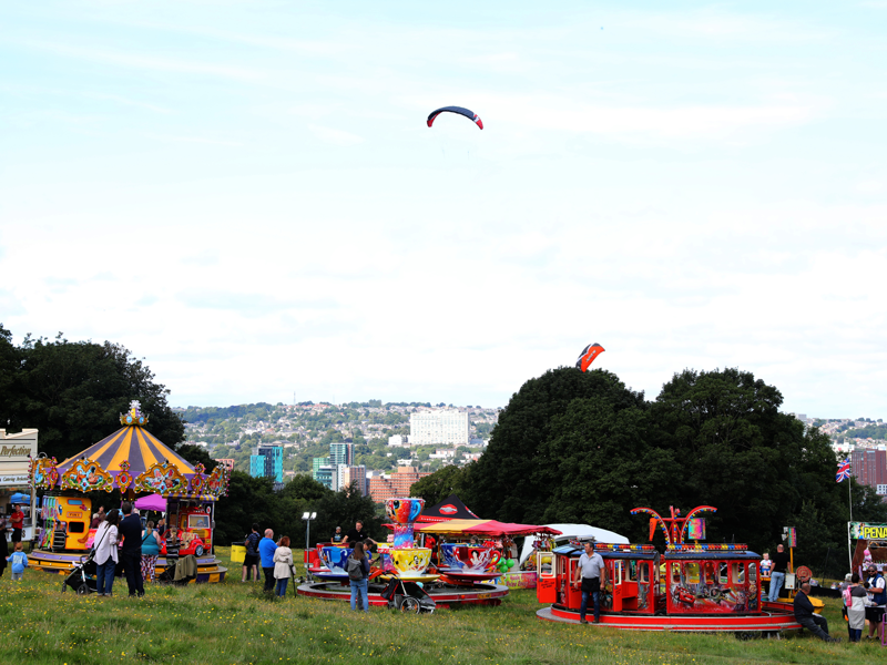 Norfolk Heritage Park with various fairground rides and people walking between them. The skyline can be seen beyond.